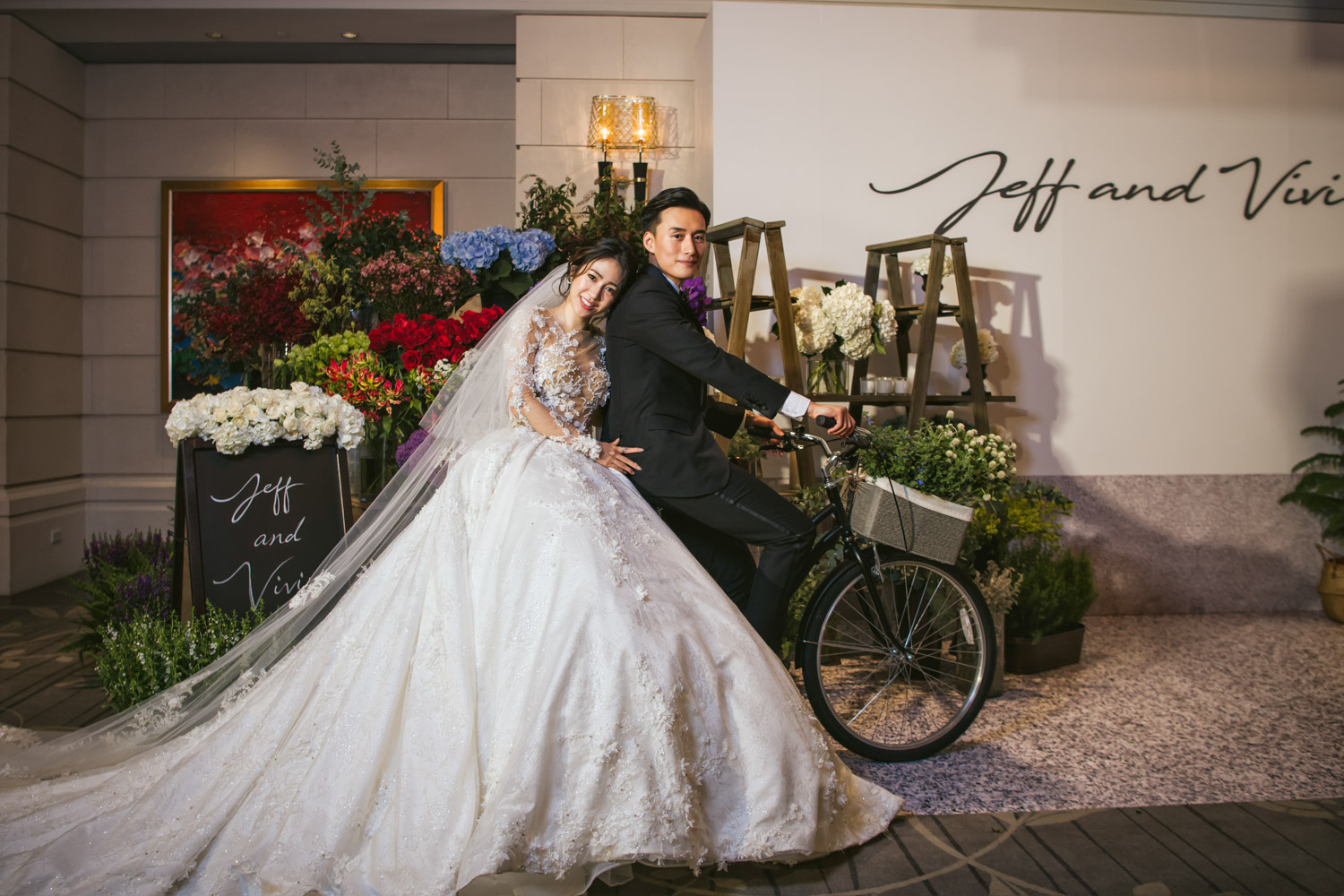 新娘穿著華麗婚紗坐在腳踏車上，新郎在一旁推車，畫面洋溢甜蜜笑意與浪漫趣味。
