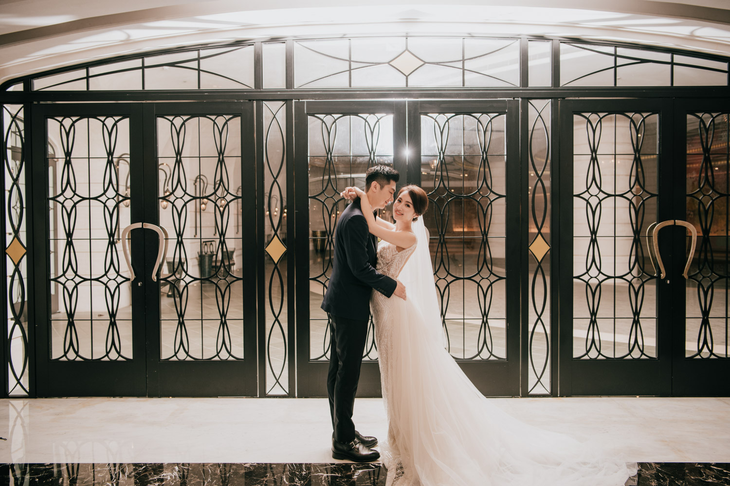 新人在典雅的大廳前深情相擁，柔和光線灑落，展現經典歐式婚禮的浪漫氛圍。